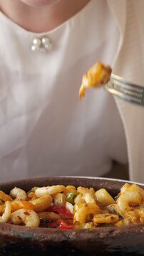 Closeup of a woman enjoying a delicious shrimp and calamari guvec, a traditional turkish seafood stew, served hot in an earthenware pot, savoring every bite with a fork in a cozy restaurant