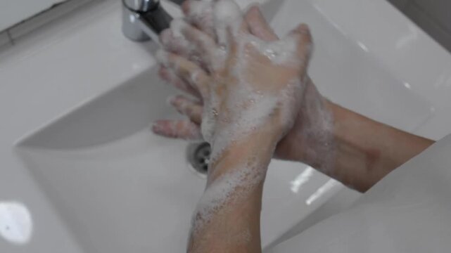 Close-up of washing hands thoroughly with a lot of white soap foam over a bathroom sink, personal hygiene and health protection concept