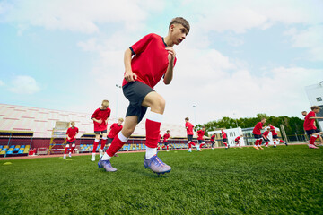 Youth soccer team running drills on stadium field. Concept of football academy practice, speed and...