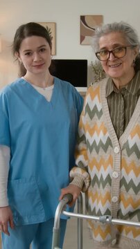 Portrait of senior woman with walker and young female caregiver smiling at camera. Clip for promoting geriatric healthcare services and nursing homes, vertical