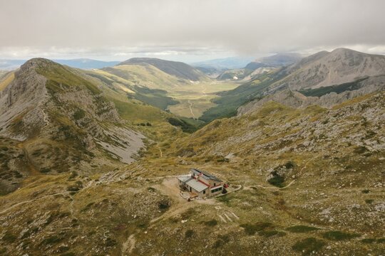 Aerial view of Piani Di Pezza featuring a mountain refuge surrounded by rugged slopes and green valleys in Rocca di Mezzo, Abruzzo, Italy.