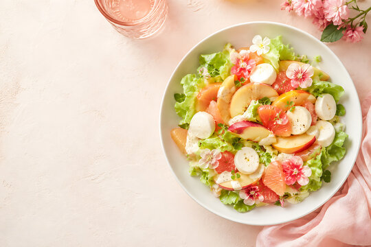 Fresh summer salad with peaches, grapefruit, mozzarella, and edible flowers on pink background
