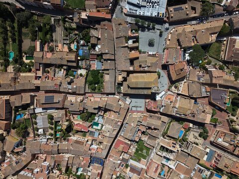 High angle drone shot of the dense urban fabric of an old historic village, showing rooftops, narrow streets, courtyards and swimming pools in a sunny day.