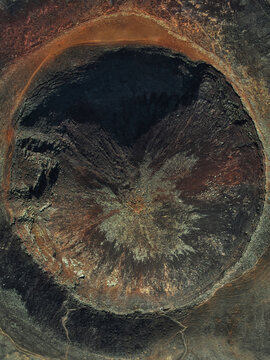 Aerial view of the volcanic crater of Calderon Hondo with rugged dark lava rock formations and steep slopes in Las Palmas, Canarias, Spain.