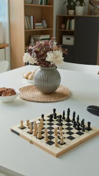 Vertical shot of chessboard with wooden pieces sitting on table next to flower vase in retirement home common room. Footage promoting senior leisure activities and care facilities