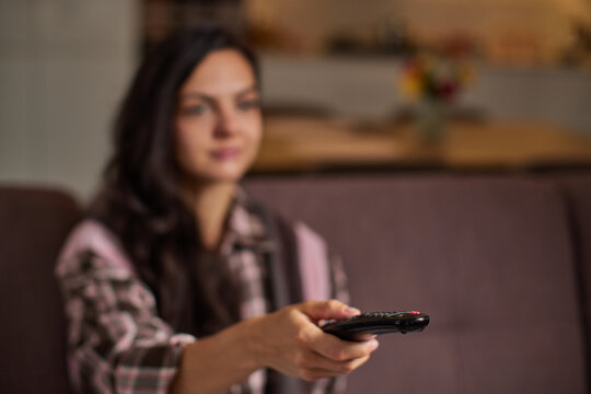 Woman holding a remote control, enjoying entertainment and leisure time in her house, focus on remote control