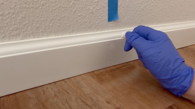 Gloved Hands Sealing Baseboard with Caulking