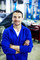 Fototapeta premium Portrait, smile and mechanic in garage with arms crossed, career and pride for engineering job. Man, confident and workshop for car repair, maintenance and auto or vehicle service specialist