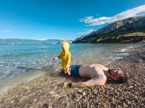 Father and toddler resting on pebble lake beach