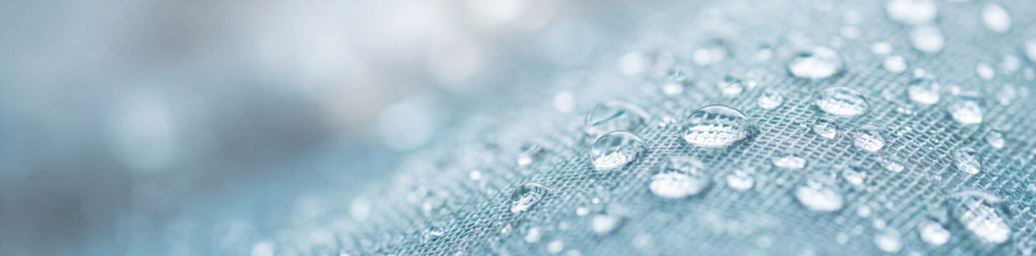 A detailed panoramic macro shot of clear round water droplets sitting on a light blue mesh fabric with a soft blurred background