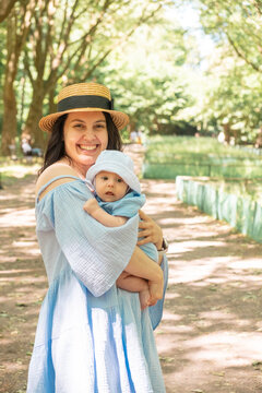 Smiling mother holding baby in sunny park portrait