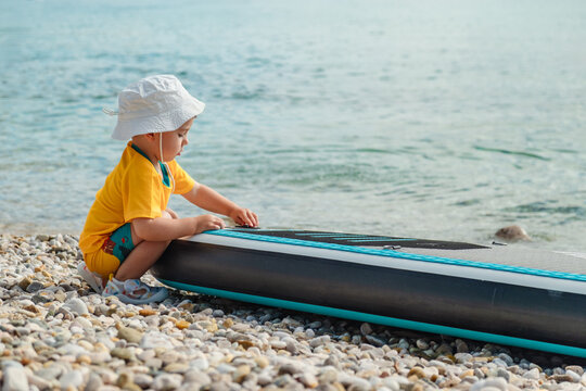 Toddler sitting by paddleboard on mountain lake beach