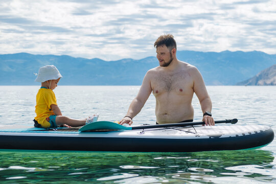 Father and toddler on paddleboard in clear mountain lake