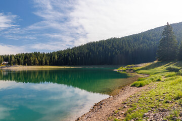 Obraz premium Calm lake with forest reflection under blue sky