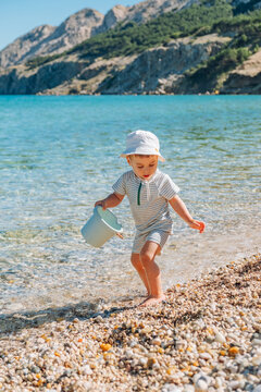 Toddler running with bucket on mountain lake beach