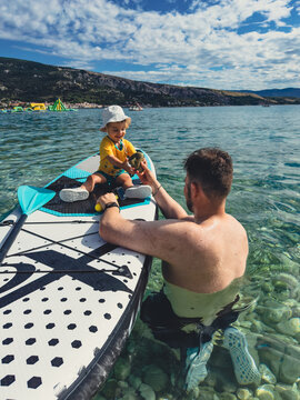 Father and toddler sitting on paddleboard in mountain lake