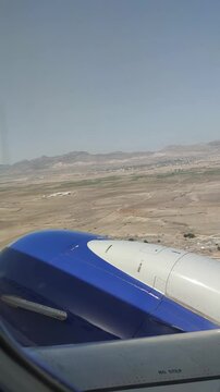 View from an airplane window looking over a blue jet engine cowling at a vast desert landscape and distant mountains below. Perfect for travel, aviation, and vacation concepts.