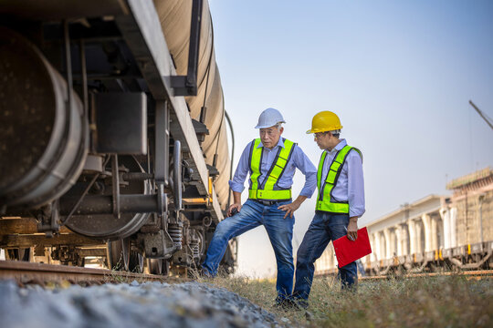Engineers inspecting a freight train tanker at railway terminal, Railway workers with hard hats and safety vests checking freight train equipment