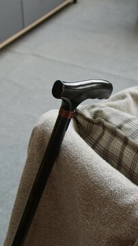 Vertical shot of walking cane leaning against armchair in retirement home. Ideal for senior care services, geriatric healthcare marketing, or retirement community advertising