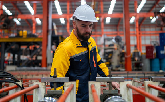Industrial engineer in safety helmet uniform jacket working in heavy steel engineering factory. Technician manager worker inspector using laptop in metalwork product manufacturing facility workplace