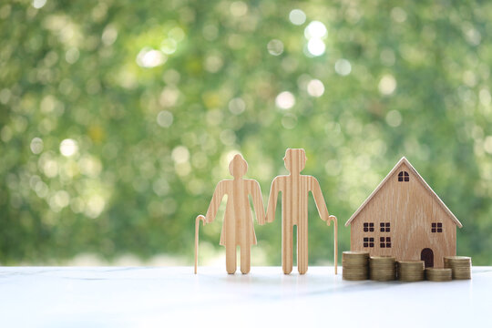 Couple wooden figures standing with a miniature house and coins, representing retirement home planning, property investment, real estate for seniors and financial security for old age.