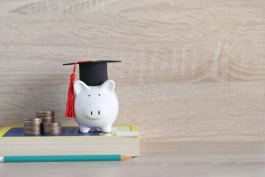 Graduation hat on blue piggy bank with stack of coins money on wooden background, Saving money for education concept