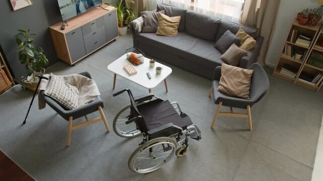 Wide angle top view shot of empty wheelchair and walking cane in retirement home living room. Footage for senior care services, medical equipment marketing, and healthcare facility ads