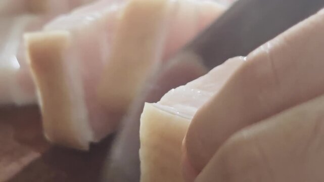 A high-quality macro close-up video capturing a person precisely slicing a piece of raw pork belly, highlighting the clean structural layers of fat, lean meat, and thick skin rind using a sharp knife