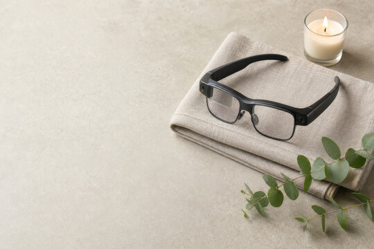 Modern smart glasses on a folded linen towel with a lit candle and eucalyptus.