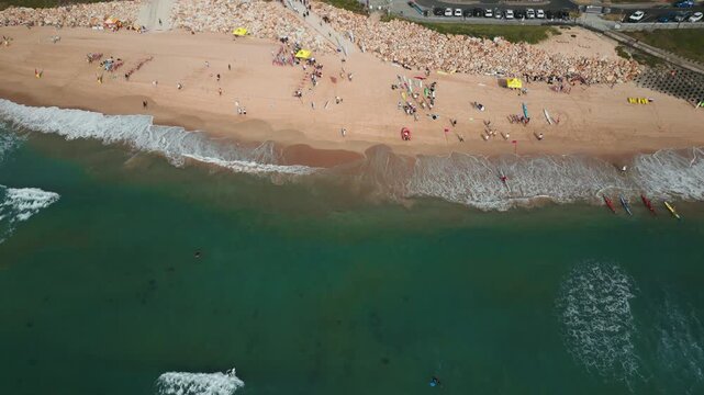 Drone view of North Cronulla Beach, Sydney, showing beachgoers, surf craft, coastal infrastructure and waves rolling onto the shoreline. Aerial shot.