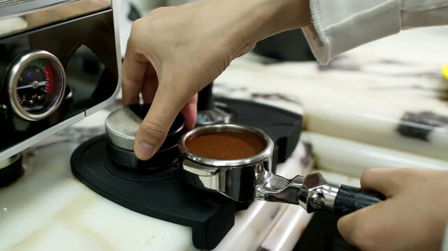 Barista tamping ground coffee in portafilter beside espresso machine on counter