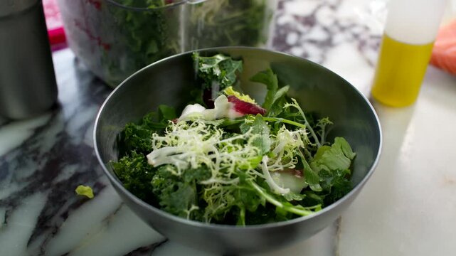 Fresh green salad with shredded cheese in a metal bowl on a marble countertop