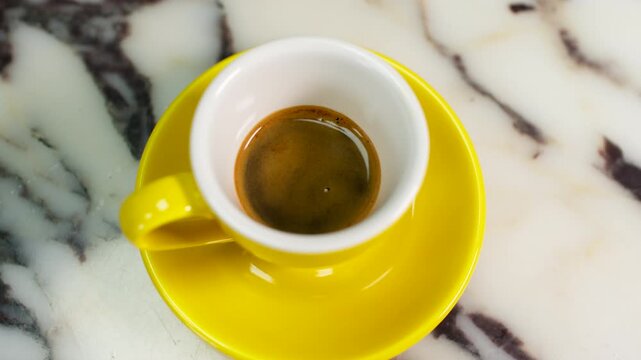 Fresh espresso served in a yellow cup on a marble countertop, viewed from above