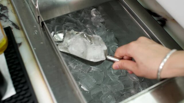 Hand scooping ice cubes from metal bin in a commercial kitchen or bar setting