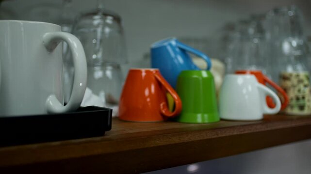 Hand picking up a colorful mug from a kitchen shelf with assorted cups and glasses