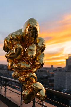 Bundle of gold heart shaped balloons on rooftop terrace at beautiful sunset over city