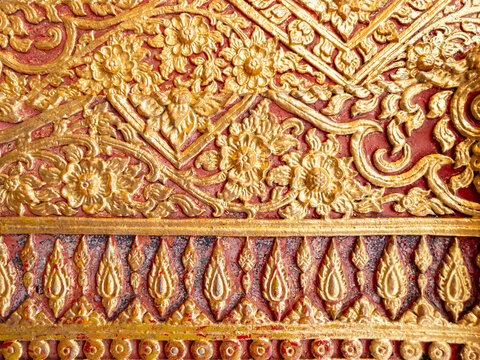 Traditional Thai golden stucco floral pattern on red wall background.