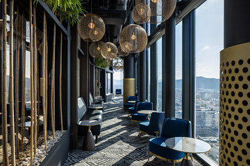 Obraz premium Stylish hotel rooftop bar with panoramic glass windows elegant blue velvet chairs and golden lamps