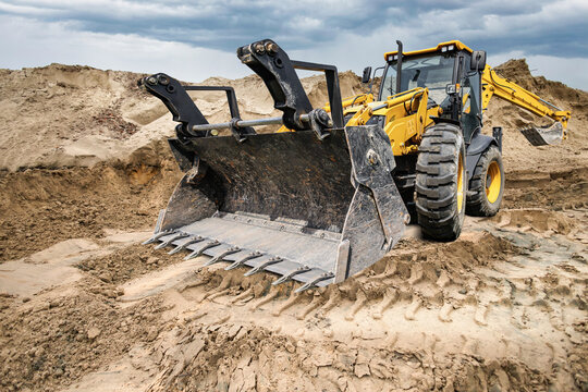 Universal excavator loader is performing work on a construction site. The machine is moving dirt and sand from one area to another during the day