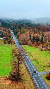 Smooth asphalt road passing the countryside with valleys and forests. Red car drives through the area in the Mount Rainer National park, Washington State, the USA. Top view. Vertical video