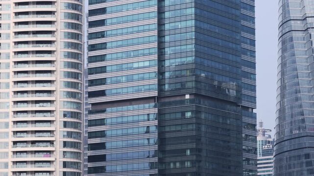 A modern glass office tower flanked by residential high-rises, showcasing reflective curtain-wall windows, repeating geometric patterns and urban density in a downtown business district landscape