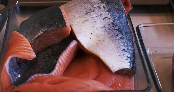 Slices of raw salmon fish with pink flesh and dark skin arranged in a glass dish