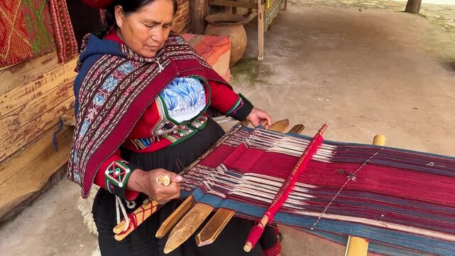 Indigenous woman in traditional clothing demonstrates the ancient art of weaving a colorful textile