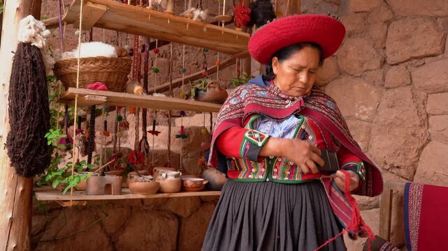 Peruvian woman in traditional dress using phone and spinning wool yarn in a workshop