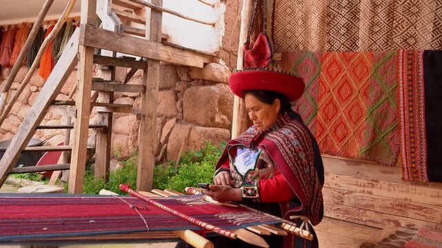 Peruvian woman answers a phone call while weaving textiles on traditional loom in a workshop