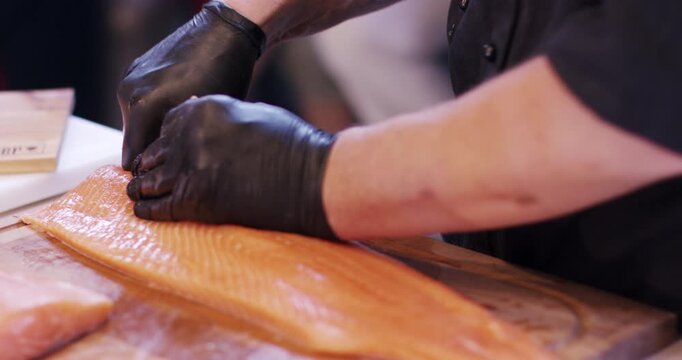 A person wearing black gloves pulls a bone from a fresh pink salmon fillet on a wooden board