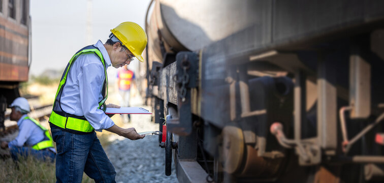 Engineer inspecting a freight train tanker at a railway terminal, Railway worker with hard hat and safety vest checking freight train equipment