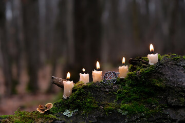 Obraz premium Burning wax candles and witch pentacle amulet close up on mossy tree trunk, natural dark forest background. magical candles for witchcraft, esoteric ritual. mystery fairy tale scene. Practical magic