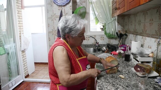  Mujer mayor cortando migas de pan para una receta tradicional de alb&oacute;ndigas. Abuela mayor cortando migas de pan en la cocina para una receta casera de alb&oacute;ndigas. Cocina tradicional, aut&eacute;ntica vida