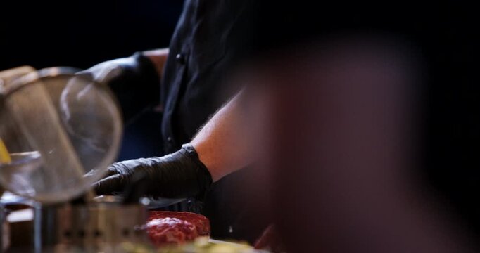 Close up view of a chef wearing black gloves preparing raw meat on a kitchen counter